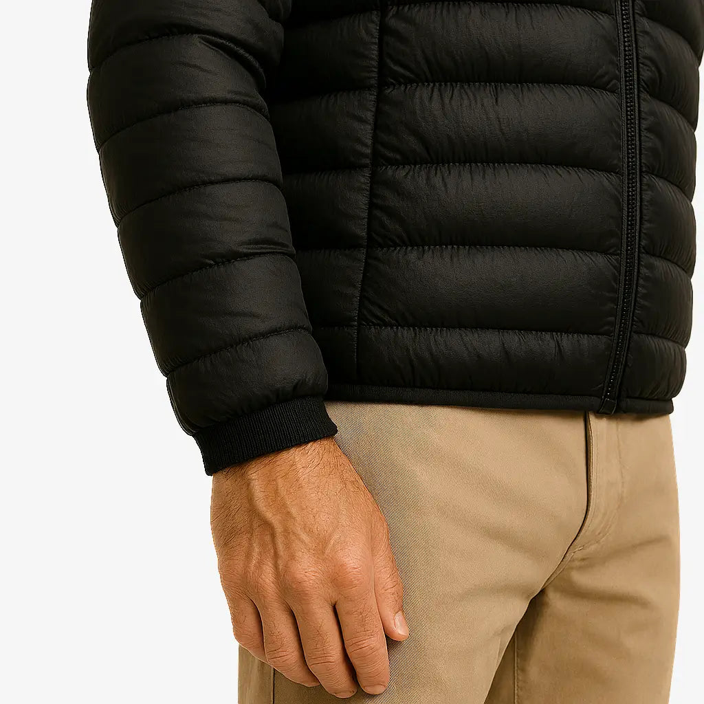 Homem vestindo jaqueta puffer masculina preta com capuz, impermeável e com zíper frontal, ideal para o inverno.