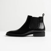 bota chelsea masculina de couro polido preto com elástico lateral e bico fino – estilo elegante sobre superfície de madeira
