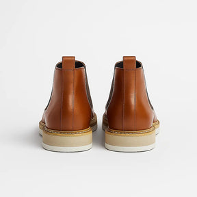 Bota Chelsea em couro legítimo com elástico lateral e solado branco.