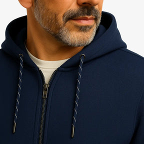 Homem vestindo blusa moletom masculina azul marinho com capuz e zíper, estilo casual urbano para dias frios, com mãos nos bolsos e camiseta branca por baixo.
