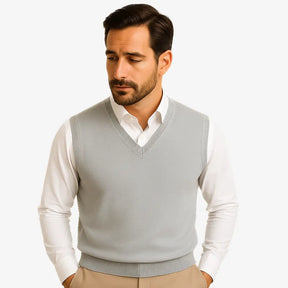 Homem usando colete masculino tricot slim cinza com gola V sobre camisa preta. Peça leve e elegante para dias de frio moderado.