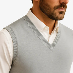Homem usando colete masculino tricot slim cinza com gola V sobre camisa preta. Peça leve e elegante para dias de frio moderado.