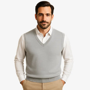 Homem usando colete masculino tricot slim cinza com gola V sobre camisa preta. Peça leve e elegante para dias de frio moderado.