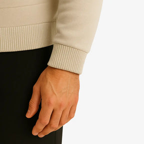 Homem usando suéter masculino bege com zíper e detalhe em relevo no peito, gola careca canelada e bolso lateral, ideal para outono/inverno.